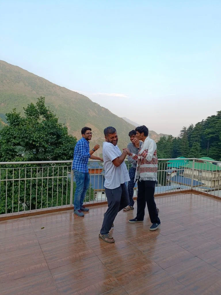 The image shows a group of digital nomads laughing and chatting at NomadGao Dharamkot