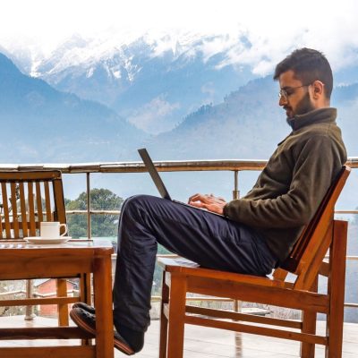 The image shows a digital nomad working remotely from NomadGao Plum Paradise Naggar Himachal India