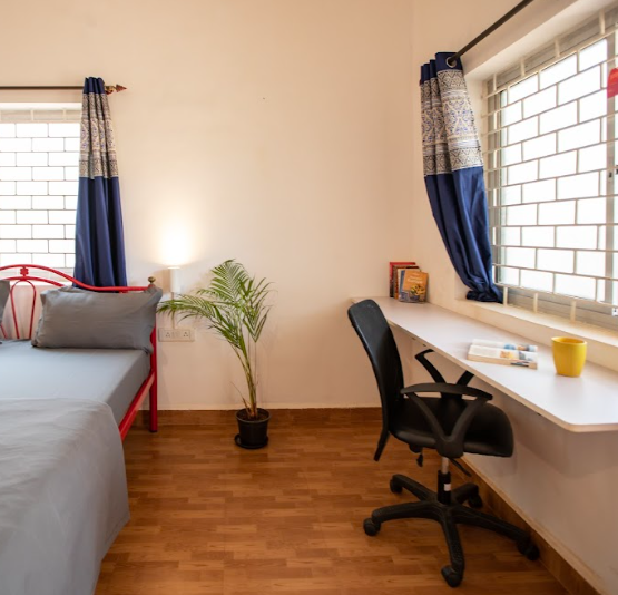 coliving space in goa india the image shows a bed with a small table and ergonomic chair on the right